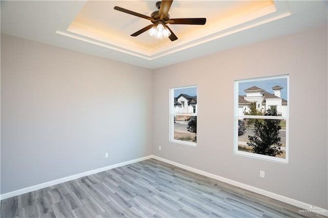 unfurnished room with light hardwood / wood-style flooring, a raised ceiling, and ceiling fan