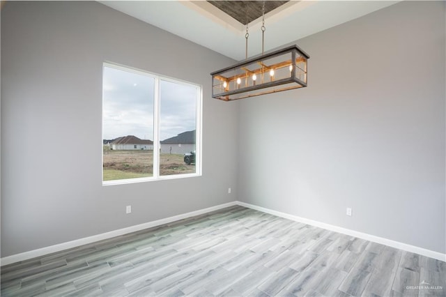 spare room featuring a raised ceiling, an inviting chandelier, and light wood-type flooring