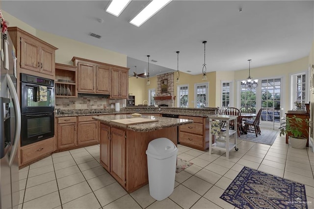 kitchen with hanging light fixtures, double oven, kitchen peninsula, a kitchen island, and ceiling fan with notable chandelier