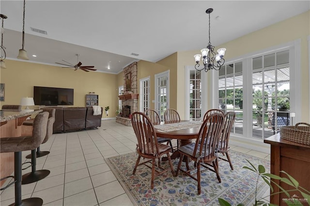 tiled dining space with ceiling fan with notable chandelier and a stone fireplace