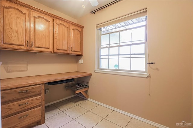 unfurnished office featuring ceiling fan, baseboards, built in desk, and light tile patterned flooring