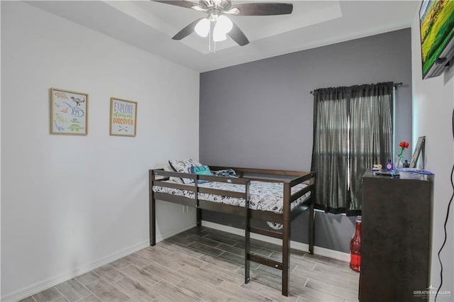 bedroom featuring baseboards, wood finished floors, and a raised ceiling