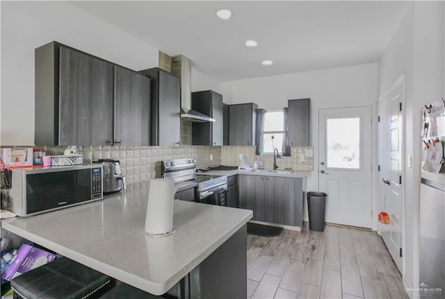 kitchen with a peninsula, wall chimney exhaust hood, tasteful backsplash, a sink, and appliances with stainless steel finishes
