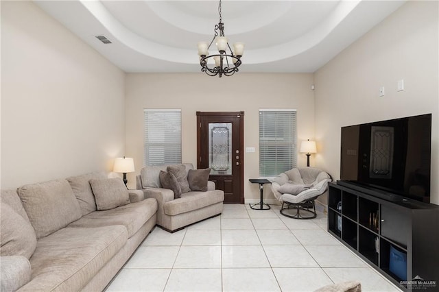 living room with light tile patterned floors, visible vents, baseboards, a tray ceiling, and a notable chandelier