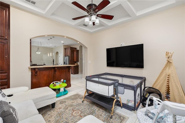 living room with light tile patterned floors, arched walkways, coffered ceiling, and a ceiling fan