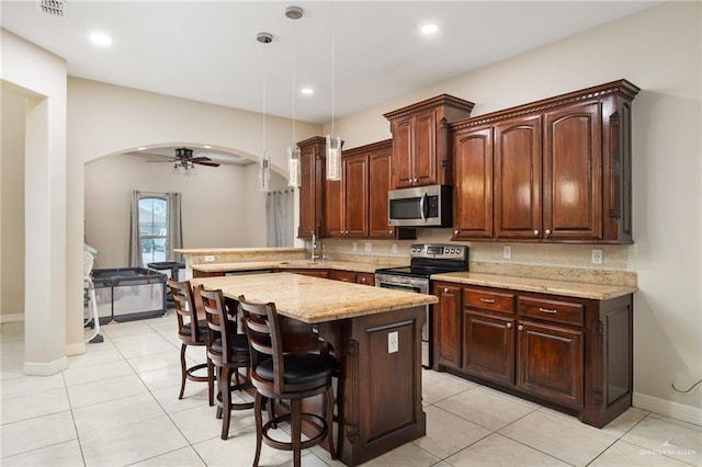 kitchen with arched walkways, appliances with stainless steel finishes, a kitchen breakfast bar, a peninsula, and pendant lighting