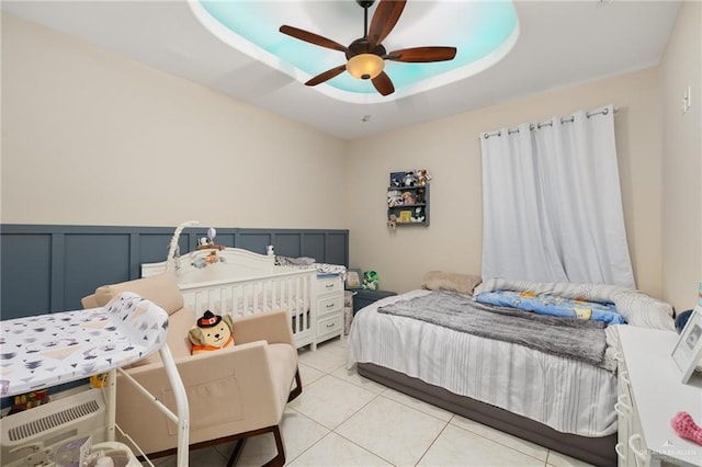 bedroom with wainscoting, a decorative wall, a ceiling fan, and light tile patterned flooring