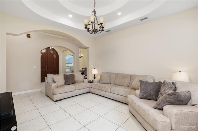 living area featuring arched walkways, light tile patterned floors, visible vents, a tray ceiling, and an inviting chandelier