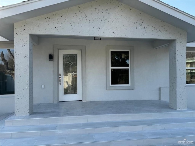 doorway to property featuring covered porch and stucco siding