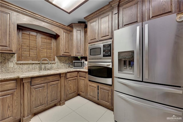 kitchen featuring light tile patterned floors, decorative backsplash, light stone counters, appliances with stainless steel finishes, and a sink