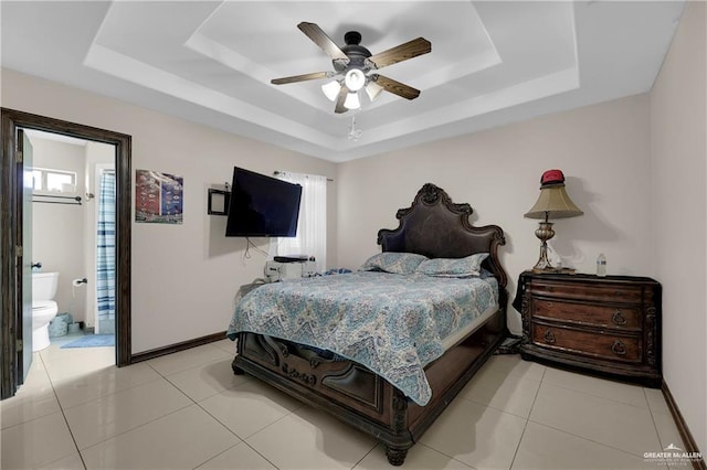 bedroom featuring light tile patterned floors, baseboards, a raised ceiling, and ensuite bathroom