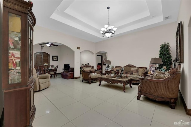 living area with visible vents, ceiling fan with notable chandelier, light tile patterned flooring, arched walkways, and a raised ceiling