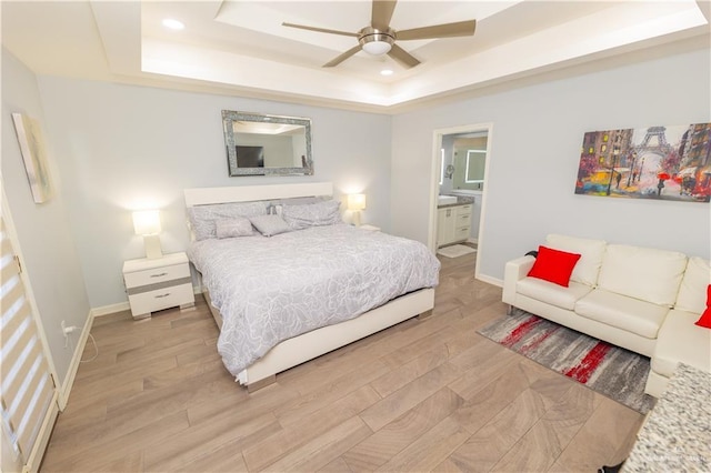 bedroom featuring baseboards, ensuite bathroom, a tray ceiling, light wood-style floors, and recessed lighting