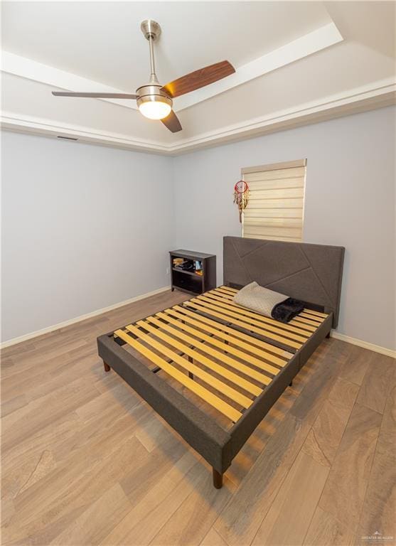 bedroom with ceiling fan, wood finished floors, visible vents, baseboards, and a raised ceiling