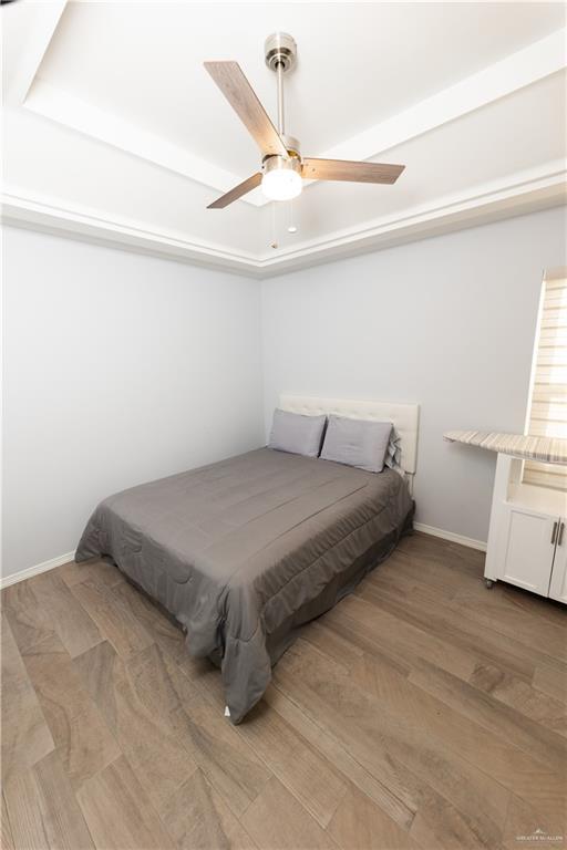 bedroom with a tray ceiling, ceiling fan, baseboards, and wood finished floors