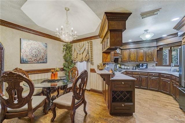 kitchen featuring a textured ceiling, light hardwood / wood-style floors, decorative light fixtures, and ornamental molding