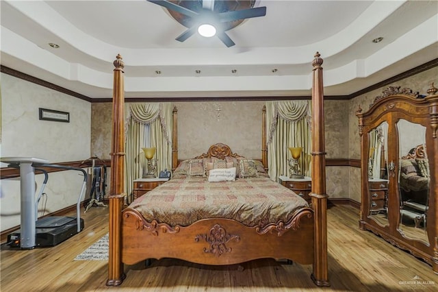 bedroom with hardwood / wood-style flooring, ceiling fan, a raised ceiling, and crown molding
