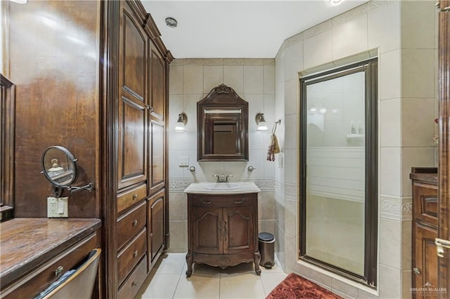 bathroom featuring tile patterned floors, a shower with door, vanity, and tile walls