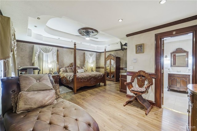 bedroom with a raised ceiling, connected bathroom, and light hardwood / wood-style flooring