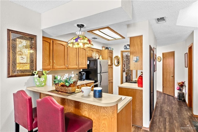 kitchen featuring kitchen peninsula, a textured ceiling, hanging light fixtures, and dark wood-type flooring