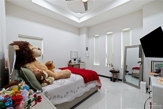 bedroom featuring a raised ceiling, light tile patterned floors, and ceiling fan