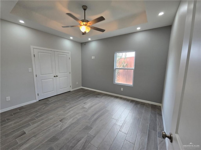 unfurnished bedroom with a closet, hardwood / wood-style flooring, a raised ceiling, and ceiling fan