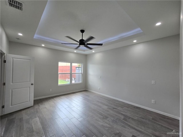 empty room with a tray ceiling, ceiling fan, and dark hardwood / wood-style flooring