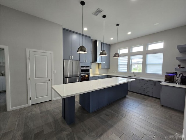 kitchen with pendant lighting, dark wood-type flooring, sink, a kitchen island, and stainless steel appliances