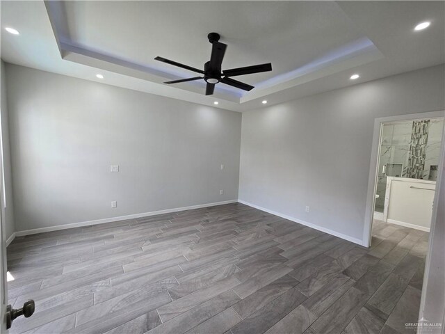 unfurnished room with wood-type flooring, a tray ceiling, and ceiling fan