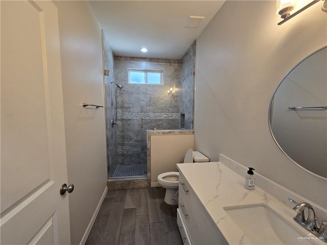 bathroom with hardwood / wood-style floors, toilet, a tile shower, and vanity