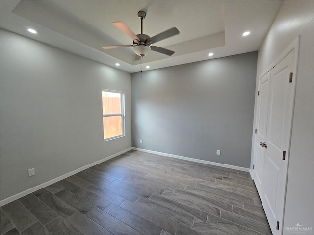 unfurnished room with a tray ceiling, ceiling fan, and dark wood-type flooring