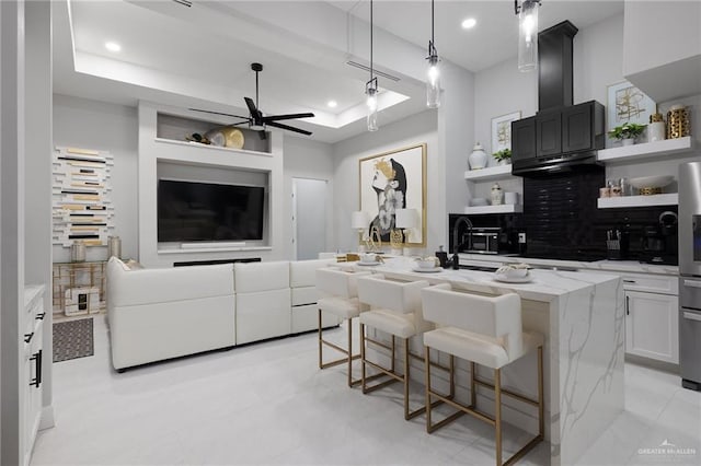 kitchen with a raised ceiling, a kitchen island with sink, a breakfast bar, and white cabinets