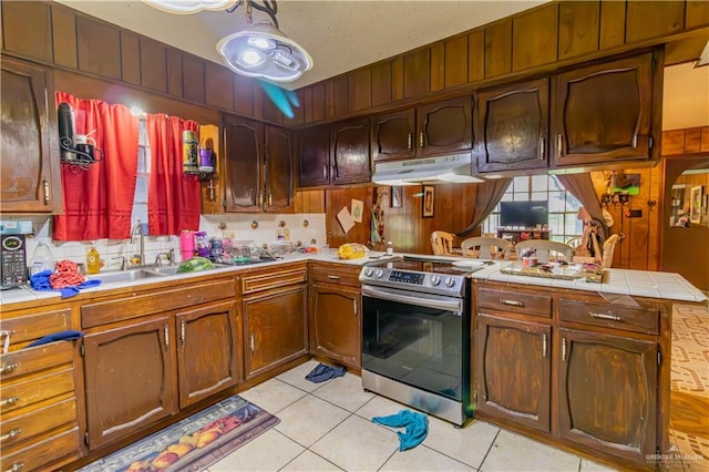 kitchen featuring sink, kitchen peninsula, stainless steel range with electric stovetop, decorative backsplash, and light tile patterned floors