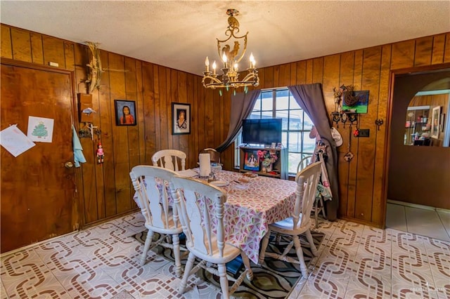 dining room with wood walls, a textured ceiling, and an inviting chandelier