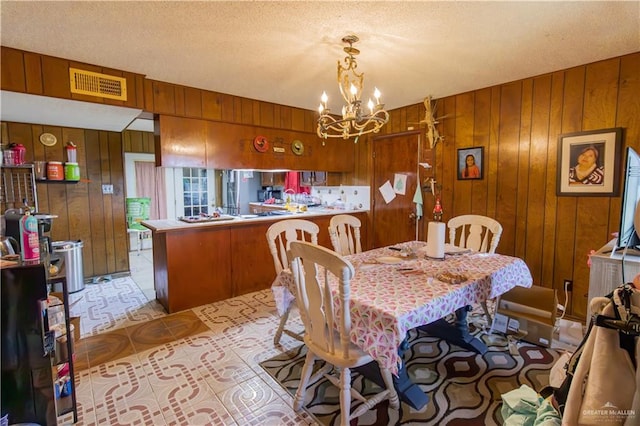 dining room with a textured ceiling, an inviting chandelier, and wood walls