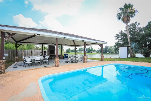 view of pool featuring a water view, a storage shed, a gazebo, a fireplace, and a patio