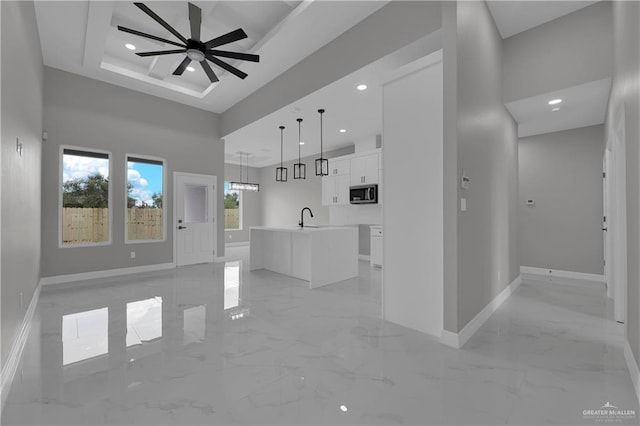 interior space featuring pendant lighting, white cabinets, sink, ceiling fan, and an island with sink