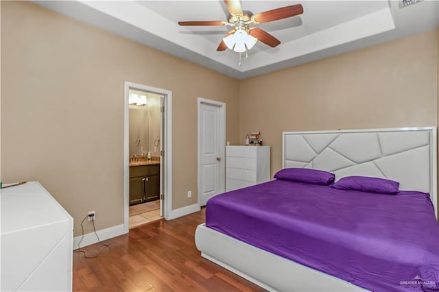 bedroom featuring ceiling fan, a raised ceiling, wood-type flooring, and ensuite bathroom