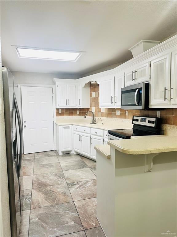 kitchen featuring a breakfast bar, white cabinetry, stainless steel appliances, decorative backsplash, and kitchen peninsula