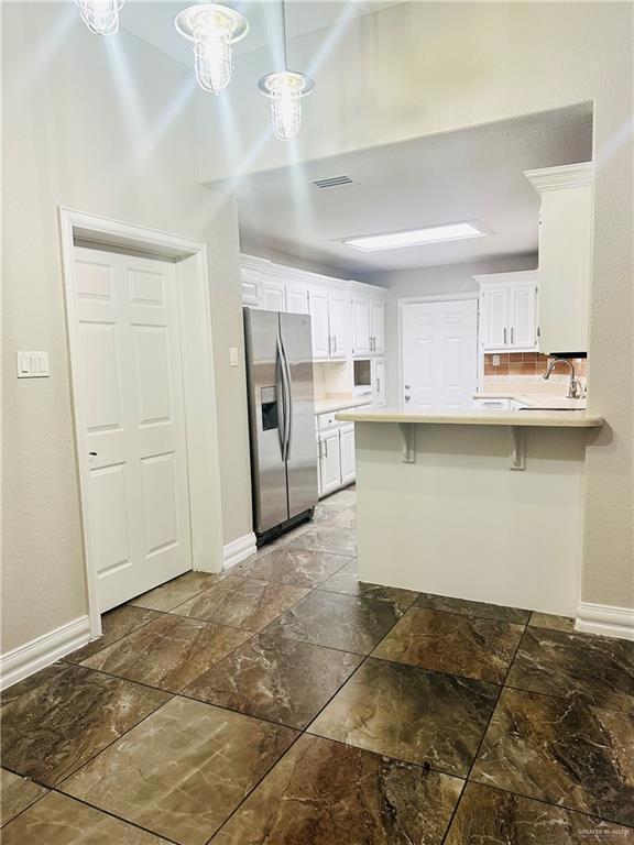 kitchen with white cabinetry, stainless steel fridge, a kitchen breakfast bar, and kitchen peninsula