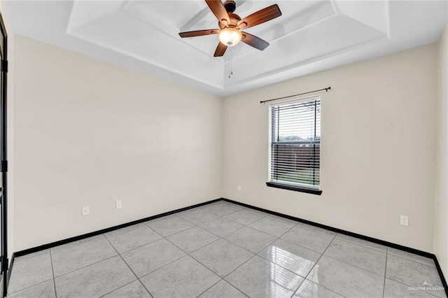 empty room with ceiling fan, a raised ceiling, and light tile patterned floors