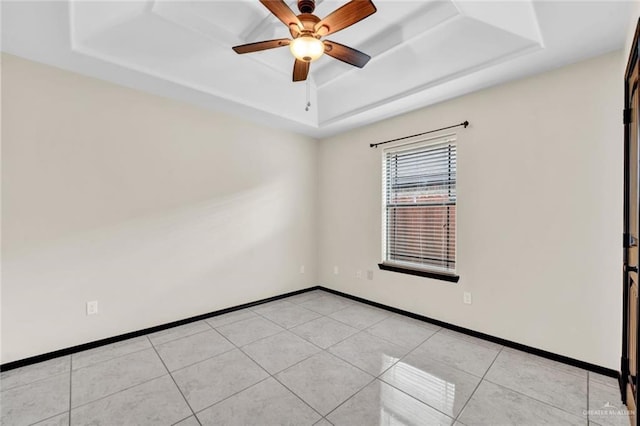 tiled empty room featuring a raised ceiling and ceiling fan