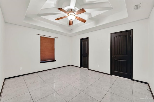 tiled empty room featuring ceiling fan and a tray ceiling