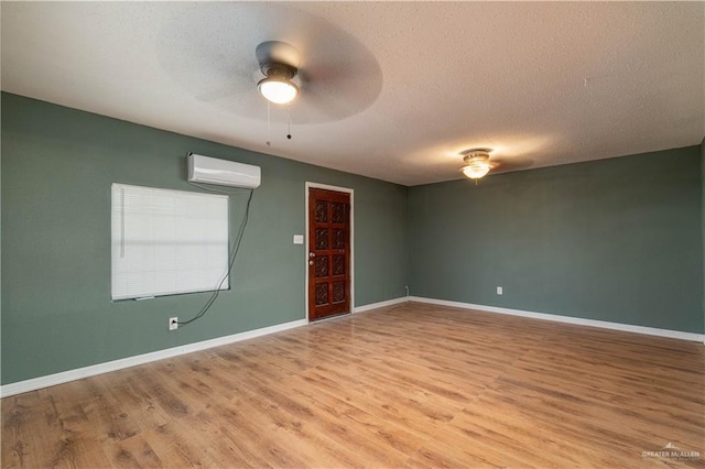 empty room featuring a textured ceiling, light wood-type flooring, a wall mounted AC, and ceiling fan