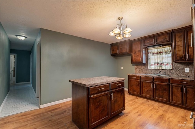 kitchen with a textured ceiling, sink, light hardwood / wood-style flooring, a chandelier, and a center island