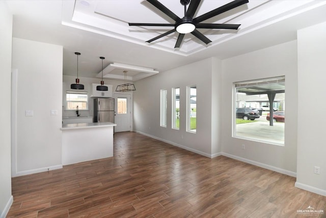 unfurnished living room featuring a raised ceiling, ceiling fan, and dark wood-type flooring