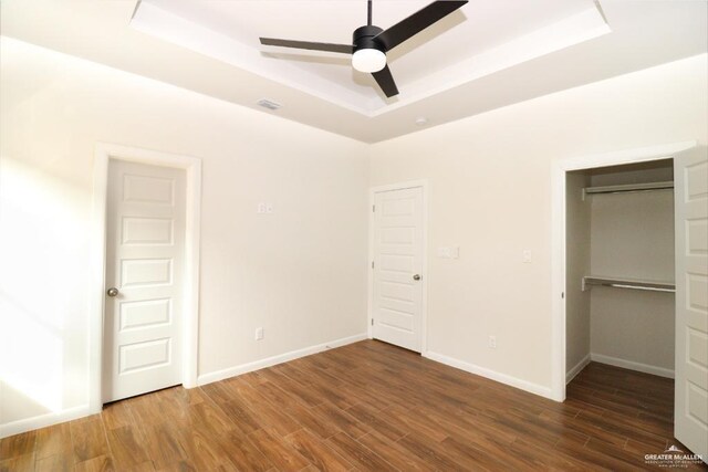 unfurnished bedroom with a tray ceiling, ceiling fan, and dark wood-type flooring