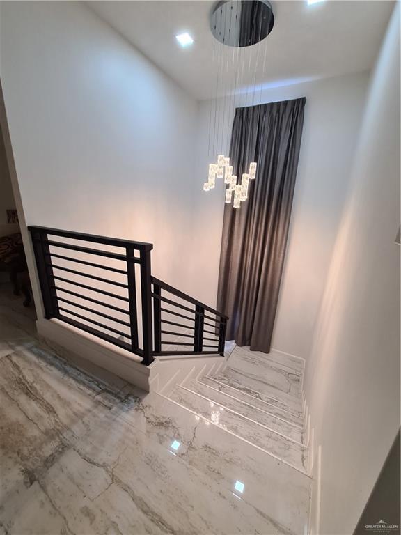 stairway featuring marble finish floor and a chandelier