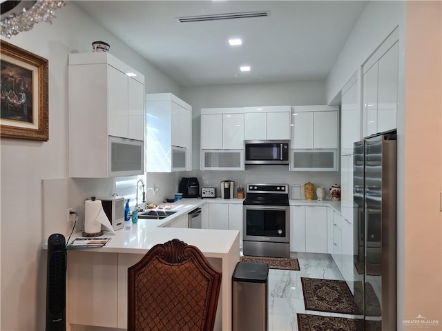 kitchen featuring appliances with stainless steel finishes, modern cabinets, a sink, white cabinets, and a peninsula