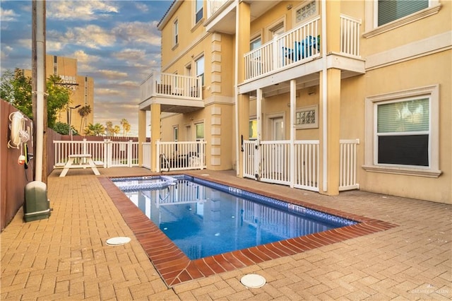 pool at dusk with a hot tub and a patio area